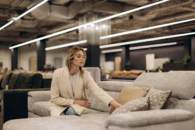 Mobilya mağazasında modern bir koltukta oturan şık bir kadın rahat bir tasarım ve estetik sergiliyor ve yastıkların kalitesini değerlendiriyor..