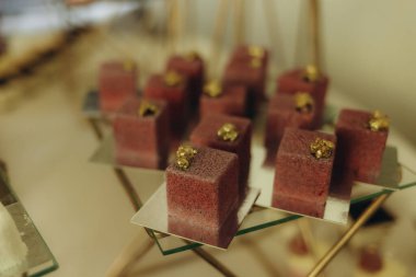 A selection of cube-shaped gourmet desserts elegantly garnished with gold flakes, displayed on geometric platters, creating a modern and luxurious presentation suitable for celebrations and special events. clipart