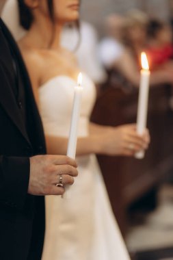 Bir gelin ve damat kilisede resmi bir düğün töreninde mum tutarlar. Odak, etkinliğin romantik ve törensel atmosferini vurgulayarak mumları vurguluyor..