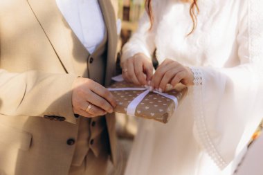 Resmi giyinmiş bir gelin ve damat, kalp desenli güzel bir hediye kutusu taşıyarak düğün günlerinde aşkı ve kutlamayı simgeliyor..