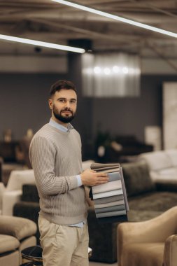 Modern mobilya galerisinde kumaş örnekleri tutan şık bir adam profesyonellik ve tasarım uzmanlığı sergiliyor..