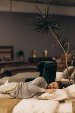 Bir adam yatakta uzanıyor, rahat görünüyor, zarif döşemelerle ve huzurlu bir ortam ile çevrili. Sahne, rafine iç dekorun ortasında huzur ve sükuneti yakalıyor..