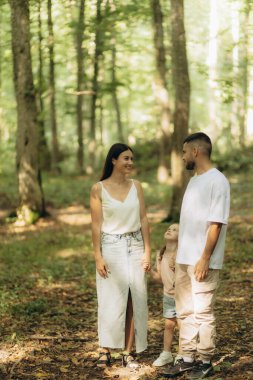 Güneşli bir günde, ormanlık bir alanda, sıcaklığı, uyumu ve doğal güzelliği sergileyen üç kişilik bir aile..