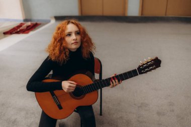 Huzurlu bir odada gitar çalan kıvırcık saçlı genç bir kadın sanatsal odaklanma ve yaratıcılığı çağrıştırıyor..