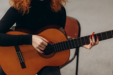 Akustik gitar çalan, yetenek ve müziği sanat ve tutku olarak vurgulayan kırmızı tırnaklı bir müzisyenin ellerine yakından bakmak. Basit arkaplan sanatsal atmosferi vurgular.