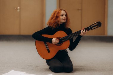 Kızıl saçlı genç bir kadın huzurlu bir iç mekanda akustik gitar çalar. Odanın sakin atmosferi ve odaklanmış ifadesi yaratıcılık ve müzik tutkusunu vurguluyor..