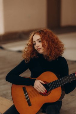 Akustik bir gitar tutan, yumuşak doğal ışık ayarında oturan, çarpıcı kızıl saçlı genç bir kadın. Düşünceli ifadesi duygu ve yaratıcılığı yansıtıyor. Müzikal tutku ve sanatsal yansıma sergiliyor..