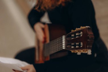 Akustik bir enstrüman tutan ve ayarlayan bir gitaristin ayrıntılı yakın çekimi, başlığı ve fretboard 'u vurguluyor, müzik alıştırması veya performans hissi uyandırıyor.