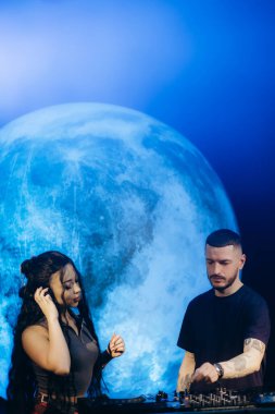 İki DJ, performanslarında yaratıcılık ve dinamik enerjiyi çağrıştıran, ay temalı parlak bir arka plan altında işbirliği yapar. Müziğe olan tutkuları, ekipmanlarıyla etkileşime geçtiklerinde belli oluyor..