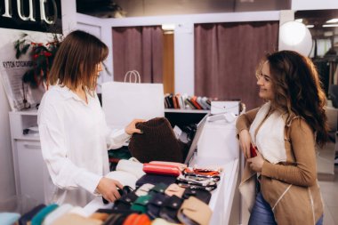 Gülümseyen bir satıcının bir butikte ürün seçerken müşteriye yardım ettiği sıcak bir sahne. Perakende satış, müşteri hizmetleri ve keyifli bir ortamda dostça bir alışveriş deneyimi..