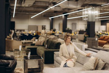 Şık oturma seçenekleri olan modern bir iç mekan ve koltuğu test eden zarif tasarımı ve rahat ambiyansı ön plana çıkaran bir kadın..