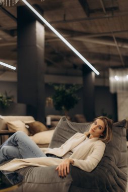 Sakin bir kadın şık, çağdaş bir iç mekâna kurulmuş rahat bir kanepede dinlenir. Dekor ve ince ışıklandırmayla vurgulanır..