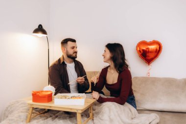 Romantik bir atmosferi olan sıcak bir suşi yemeğini paylaşan çift, buna kalp şeklinde bir balon da dahil. Sıcak ortam ve ifadeler, özel ve rahat bir ortamda sevgi, birliktelik ve neşe gösteriyor..