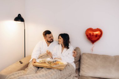 Beyaz cüppeli, sevgi dolu bir çift romantik atmosferli rahat bir ortamda suşi yer, şefkat ve rahatlığı ön plana çıkarır..