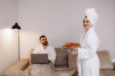 Evde pizza ve rahatlama ile bir anı paylaşan bir çiftin samimi bir sahnesi..