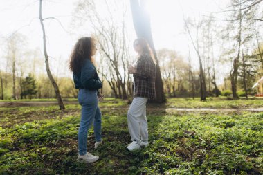Çevresi yeşilliklerle çevrili iki kişi gün ışığında bir orman parkında dikilip sohbet ediyorlar..