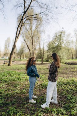İki kadın bir orman parkında dikiliyor, hoş bir günde yemyeşil ve uzun ağaçlarla çevrili tesadüfen sohbet ediyorlar..