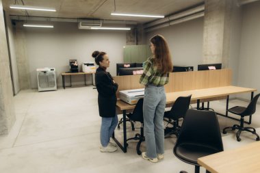 Modern ofis ortamında masa ve ofis malzemeleriyle sohbet eden iki bayan arkadaş..