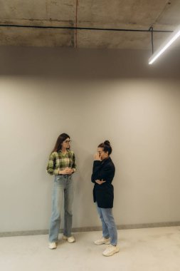 İki kadın modern ofis ortamında öylesine sohbet ediyorlar. Yakın ve profesyonelce görünmeleri, çağdaş bir çalışma ortamında etkileşime girildiğini gösteriyor..