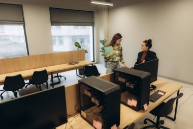 Çağdaş bir ofis ortamında işbirliği yapan iki profesyonel, masalar, bilgisayarlar ve parlak bir çalışma ortamı.