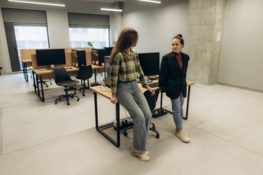 Modern çalışma istasyonları ve açık tasarım konseptinin yer aldığı çağdaş bir ofiste iki kadın, sakin ve üretken bir ortamda işbirliği ve mesleki bağlantıları teşvik ederek gelişigüzel etkileşime giriyor..