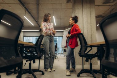 Çağdaş bir ofis ortamında sohbet eden iki kadın iletişim ve işbirliğini teşvik ediyor. Ayar, oturma düzenleri ve modern dekorlarla parlak ve profesyonelce..