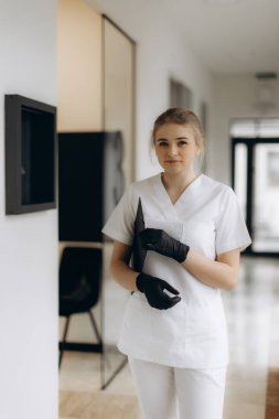 Eldiven ve üniforma giyen kendini adamış bir sağlık uzmanı çağdaş bir klinik ortamda duruyor ve tıp alanında profesyonellik ve bakım gösteriyor..