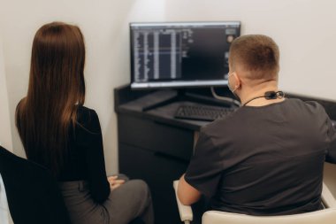 Bir hasta klinik bir ortamda bir tıp uzmanıyla buluşur, sağlıkla ilgili konuları tartışırken özel bir ofisteki bilgisayar ekranında görüntülenen elektronik sağlık kayıtlarını inceler..