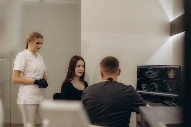 Uzman bir ekibin hastayla etkileşime girdiği ve muayene sırasında röntgen taramalarını gözden geçirdiği modern diş muayenehanesi, özel bir sağlık ortamında sağlığa odaklı bakımı vurguluyor..