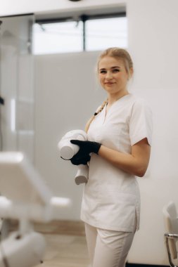 Temiz ve parlak bir diş kliniğinde gülümseyen kadın diş hekimi, profesyonel ekipman tutuyor ve eldiven takıyor, yeterlilik ve hastanın diş tedavisine özen gösteriyor..