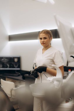 Modern, temiz bir klinikte uzman bir dişçi asistanı elinde profesyonel ekipmanla, hijyenik ve hasta dostu bir ortamda mükemmel bir hasta bakımı sağlamaya hazır ve odaklanmış bir şekilde duruyor..