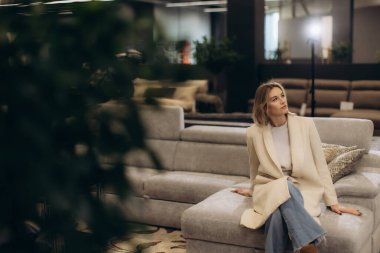Modern bir koltukta oturan zarif bir kadın. Etrafı şık, rahat bir oturma odasıyla çevrili. Atmosfer lüks ve şık, zevkli bir iç mekan içinde rahatlık ve rahatlığı vurguluyor..