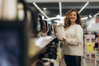 Neşeli bir kadın satın almak için çeşitli aletleri hevesle inceleyen bir elektronik mağazasını keşfediyor. Modern bir iç mekan ve geniş bir ürün seçimi ilgi çekici bir alışveriş deneyimi yaratır..