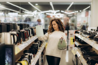 Genç bir kadın modern bir elektronik mağazasında çeşitli çaydanlık seçeneklerini araştırıyor..