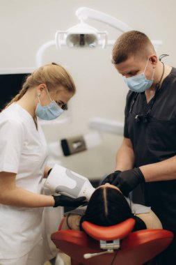 Dişçiler modern bir diş kliniğinde ileri teknolojiyle hasta bakımını ve hassasiyetini sağlamak için bir prosedür uyguluyorlar. Sağlık ekibi, güvenli bir ortamda yüksek kaliteli diş hizmetleri sunmaya odaklanmış durumda..
