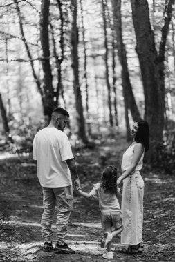 Sevgi dolu bir aile, huzurlu, yemyeşil bir ormanda el ele yürürken dışarıda kaliteli zaman geçirir. Bağlantının vurgulanması, bağ kurulması ve tek renkli ortamda doğanın güzelliği.