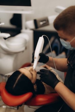 Bir diş hekimi modern bir diş kliniğinde son teknoloji ürünü ekipman kullanan bir hastayı muayene eder ve bakım ve hassasiyet sağlamaya odaklanır..