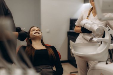 Modern bir dişçi muayenehanesindeki genç bir kadın profesyonel diş bakımı ve diş beyazlatma prosedürleri alıyor..
