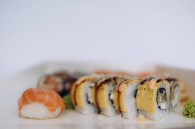 Somon nigiri 'nin altını çizen bir suşi düzeneği ve soslu benzersiz üstü suşi ruloları, temiz bir arka planda Asya mutfağının enfes bir görüntüsünü sunuyor..