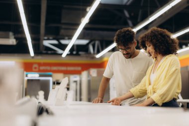 Parlak ışıklı, modern bir elektronik mağazasında birkaç ev aletine göz gezdirdim. Meşgul ve ilgili görünüyorlar. Satın alma seçeneklerini ve özelliklerini tartışıyorlar..