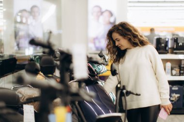 Genç bir kadın, çağdaş bir mağazada çeşitli elektronik ürünlere göz atıyor, ilgi ve özenle ürünler seçiyor, perakende deneyiminin keyfini çıkarırken tercihlerini yansıtıyor..