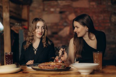 İki kadın, sıcak dekore edilmiş bir restoranda, dostluk ve neşeyi vurgulayarak keyifli bir yemek yiyorlar. Sıcak ortam deneyimi güçlendirir, sonsuz bir bağlantı ve memnuniyet anı yaratır..