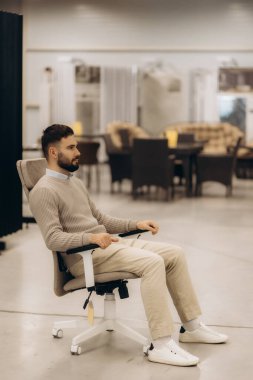Bir adam modern bir ofis koltuğunda rahatça oturup mobilya galerisinin kalitesini değerlendiriyor..