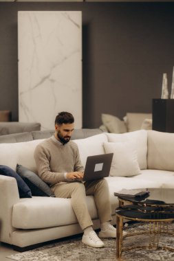 Bir insan, modern bir yaşam alanındaki rahat ve odaklanmış rahat bir koltukta otururken dizüstü bilgisayar kullanır..