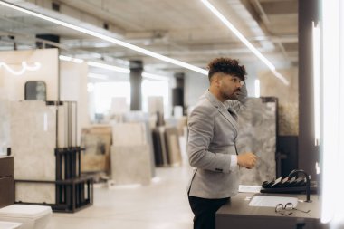 Profesyonel giyimli bir adam çağdaş bir iç tasarım galerisinde inşaat veya yenileme projesi için fayans örneklerini inceleyerek inşaat malzemelerini inceliyor..