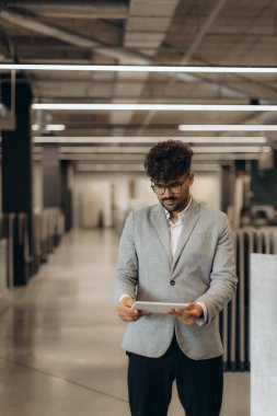 Akıllı giyimli bir adam, profesyonelliği vurgulayarak, iyi aydınlatılmış, çağdaş bir ofis ortamında bir tableti inceler..