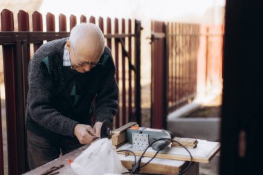 Yaşlı bir adam açık havada bir zanaat projesine odaklanır. Etrafı güneşli bahçeyle çevriliyken ahşap işçiliği için elektrikli bir alet kullanır. Kararlılığı, barışçıl bir ortamda zanaatkarlığı ve bağlılığı vurguluyor..