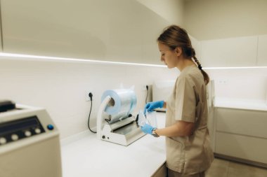 Hemşire, modern bir klinikte aletleri sterilize etmek için bir ambalaj makinesini dikkatlice kullanarak, hijyen ve hasta güvenliğini sağlıyor.