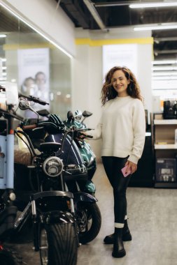 A cheerful young woman browsing stylish electronics and accessories in a well-lit retail store setting.