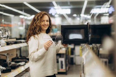 Mağazanın elektronik bölümlerini karıştıran neşeli genç bir kadın ev ihtiyaçları için modern seçenekleri araştırıyor..